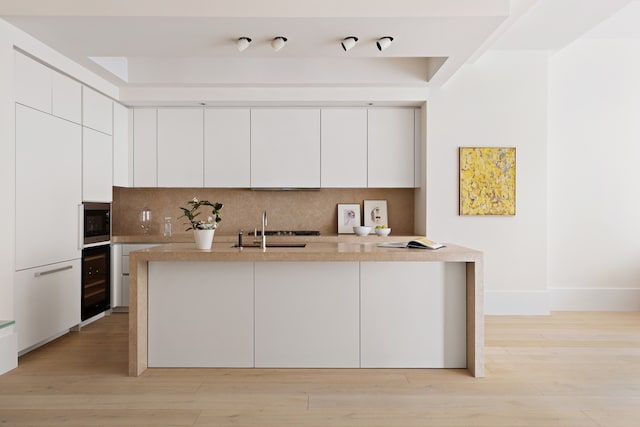 kitchen with stainless steel microwave, tasteful backsplash, a sink, beverage cooler, and modern cabinets