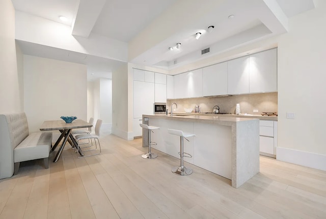 kitchen featuring a kitchen island with sink, backsplash, light wood finished floors, and modern cabinets