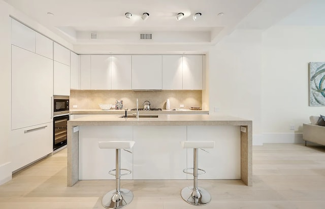 kitchen with oven, decorative backsplash, stainless steel microwave, modern cabinets, and a kitchen bar