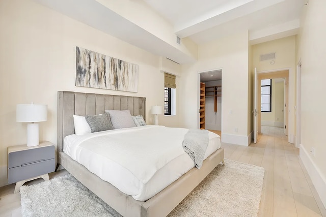 bedroom featuring a closet, light wood-type flooring, a walk in closet, visible vents, and baseboards
