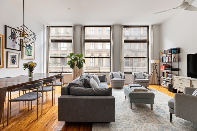 living room featuring ceiling fan with notable chandelier and light wood finished floors