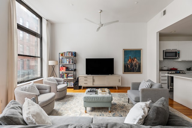 living room with a ceiling fan, floor to ceiling windows, visible vents, and wood finished floors