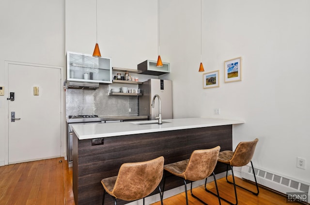 kitchen featuring tasteful backsplash, a baseboard radiator, wood-type flooring, a peninsula, and a sink