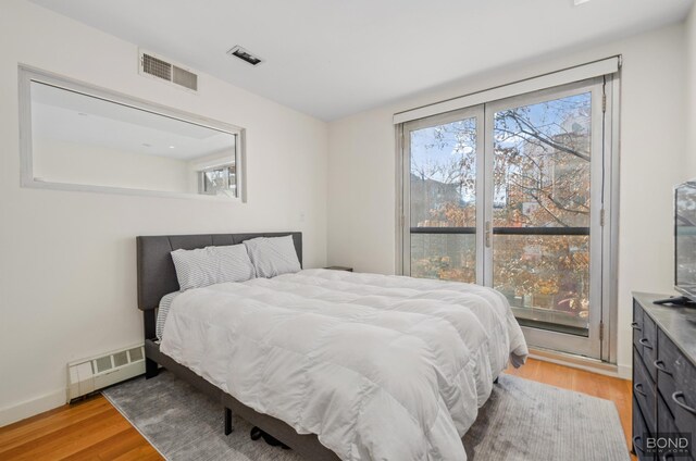 bedroom featuring a baseboard heating unit, light wood-style flooring, visible vents, and baseboards