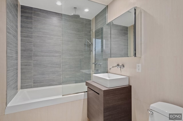 bathroom with a combined bath / shower with rainfall shower, vanity, toilet, and tile walls