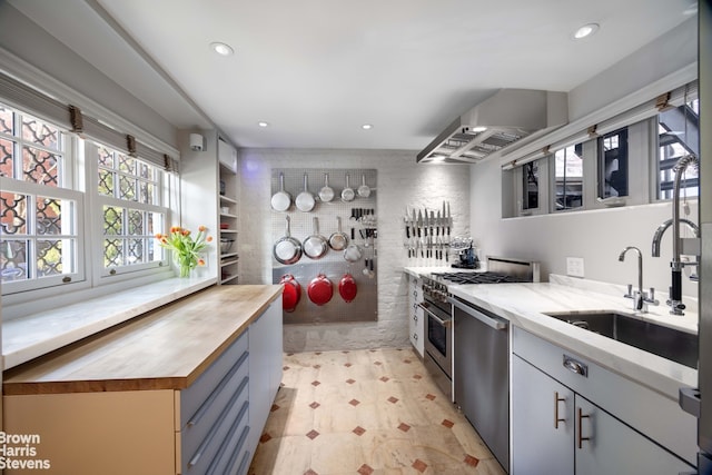 kitchen featuring stainless steel appliances, recessed lighting, a sink, butcher block countertops, and wall chimney exhaust hood