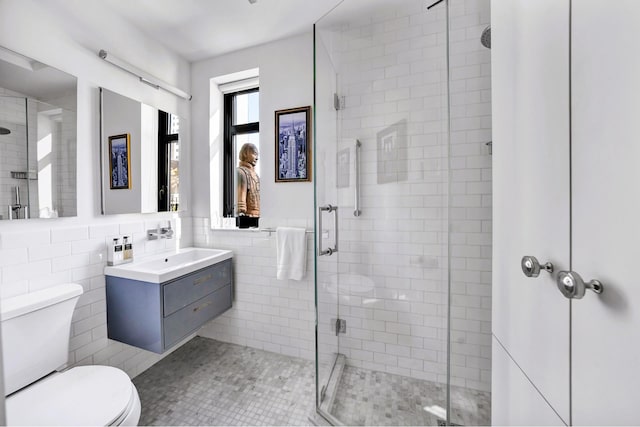 bathroom featuring tile walls, a shower stall, toilet, and vanity