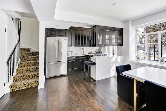 kitchen with dark wood-style flooring, high end fridge, light countertops, glass insert cabinets, and dark cabinetry