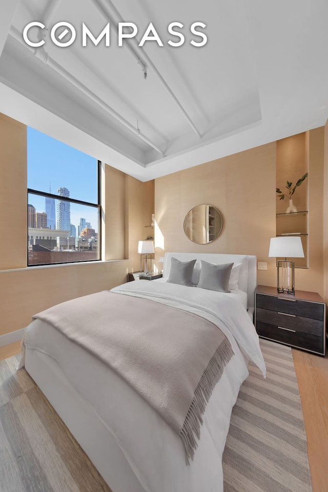 bedroom with a view of city, wood finished floors, and beamed ceiling