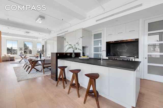 kitchen featuring a breakfast bar area, light wood-style floors, white cabinetry, dark countertops, and modern cabinets