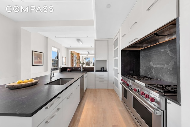 kitchen featuring dark countertops, light wood finished floors, appliances with stainless steel finishes, white cabinetry, and a sink