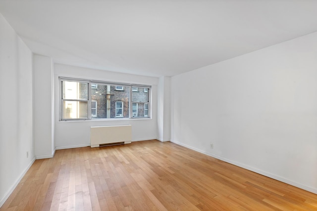 empty room featuring light wood finished floors, radiator, and baseboards