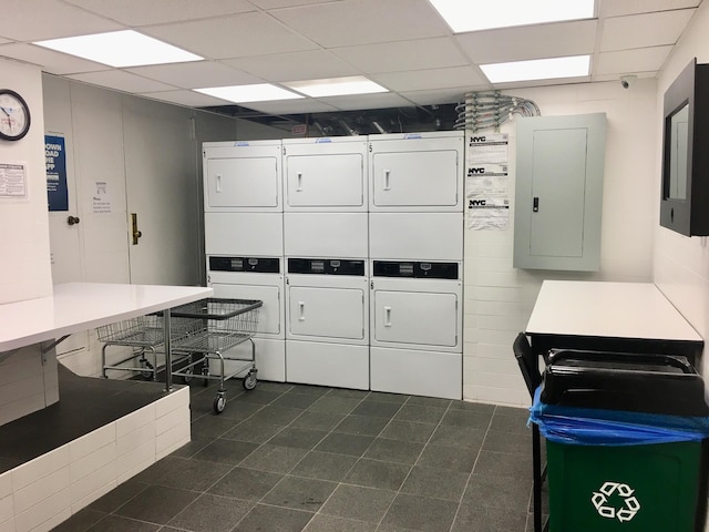 community laundry room featuring electric panel, stacked washer / drying machine, and dark tile patterned floors