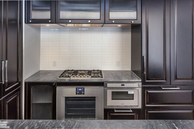 kitchen with dark brown cabinets, appliances with stainless steel finishes, glass insert cabinets, and tasteful backsplash