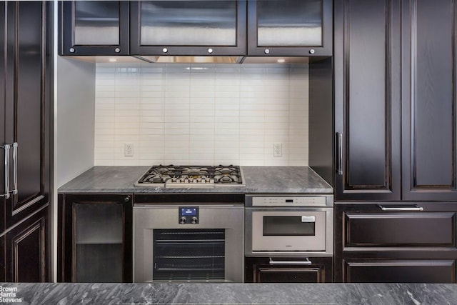 kitchen featuring glass insert cabinets, backsplash, stainless steel appliances, and dark brown cabinets