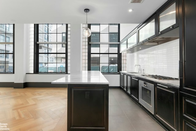 kitchen with backsplash, hanging light fixtures, stainless steel gas cooktop, baseboards, and glass insert cabinets
