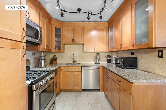 kitchen with a sink, appliances with stainless steel finishes, light stone counters, and glass insert cabinets