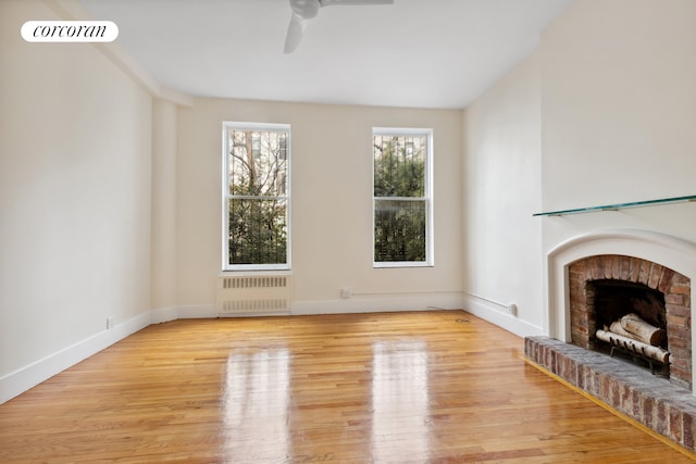 unfurnished living room featuring visible vents, radiator, a brick fireplace, baseboards, and light wood-style flooring