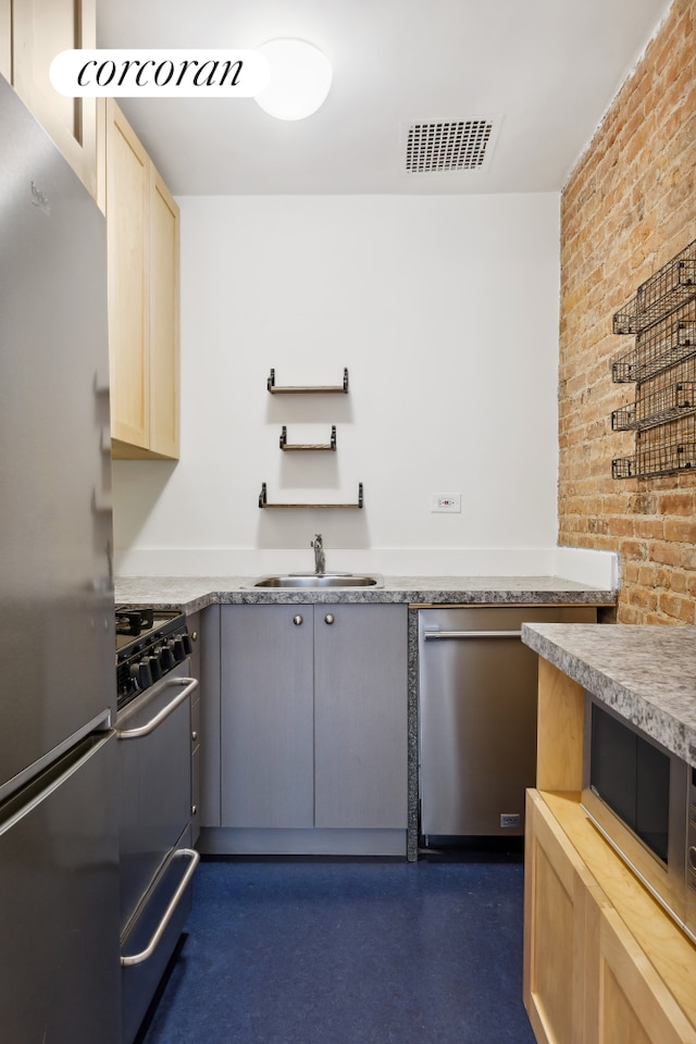 kitchen featuring brick wall, visible vents, light brown cabinetry, a sink, and stainless steel appliances