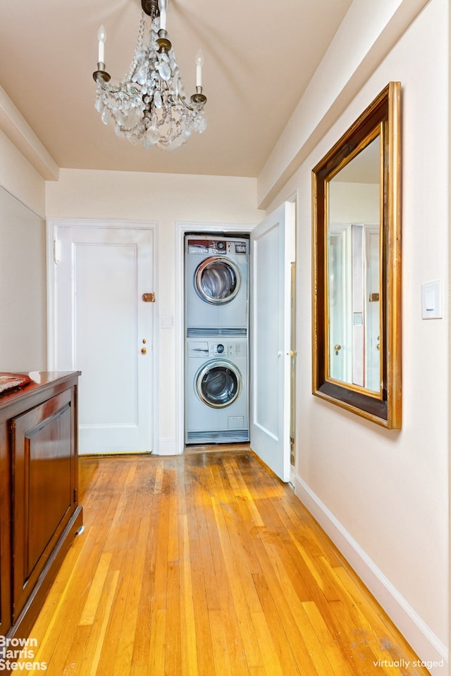 414 E 52nd St Unit 10E, New York City, NY 10022 - washroom with stacked washing machine and dryer, a chandelier, light wood-type flooring, and baseboards