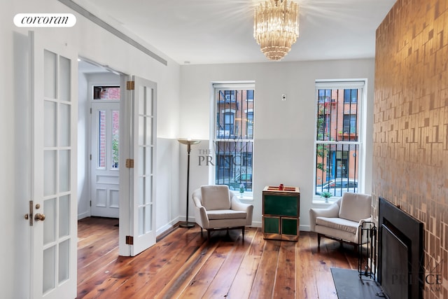 living area with visible vents, baseboards, a fireplace with flush hearth, hardwood / wood-style flooring, and a notable chandelier