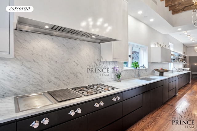 kitchen featuring wood finished floors, a sink, white cabinets, wall chimney exhaust hood, and tasteful backsplash