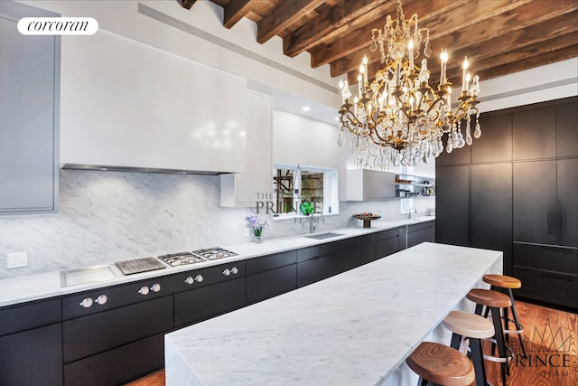kitchen with beam ceiling, a sink, a kitchen bar, modern cabinets, and tasteful backsplash