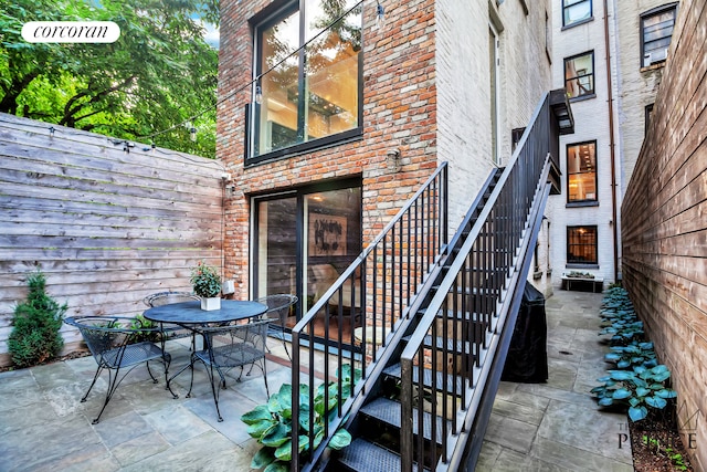 view of exterior entry with a patio, outdoor dining area, fence, and brick siding