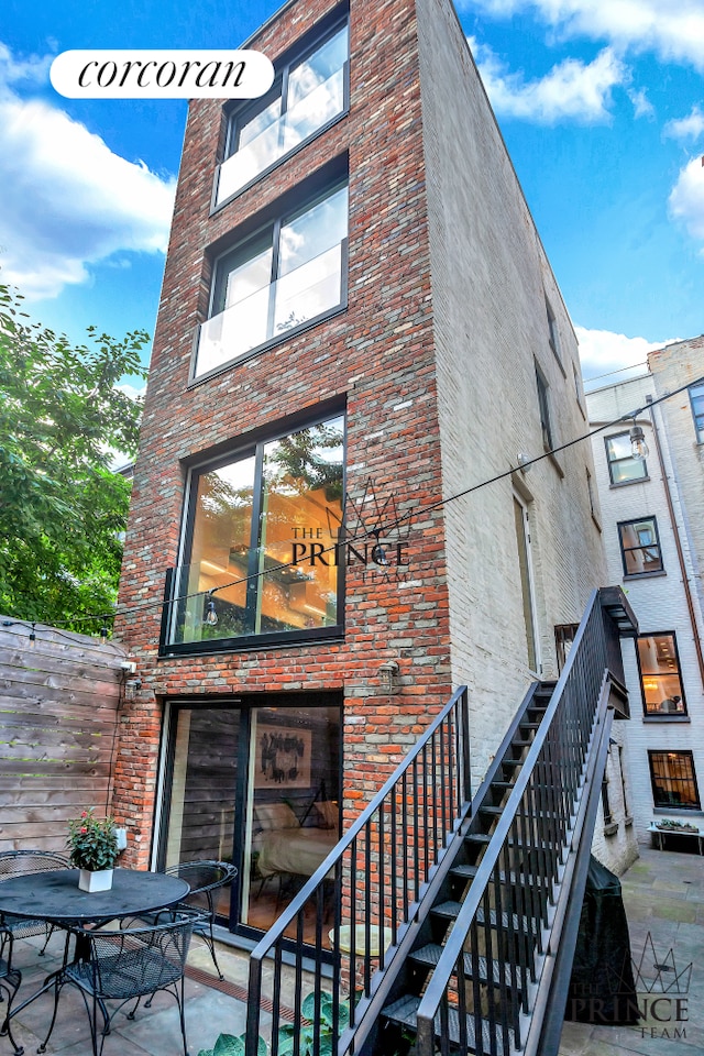 back of house featuring brick siding, stairway, and a patio area