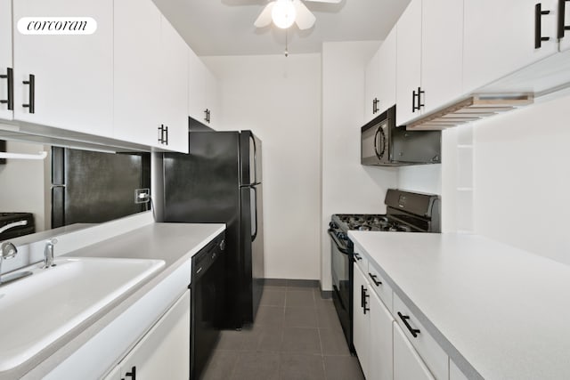 kitchen with dark tile patterned floors, light countertops, white cabinets, black appliances, and a sink