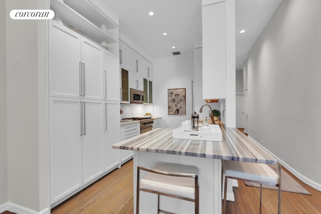 kitchen featuring light wood finished floors, a peninsula, white cabinets, appliances with stainless steel finishes, and a kitchen bar