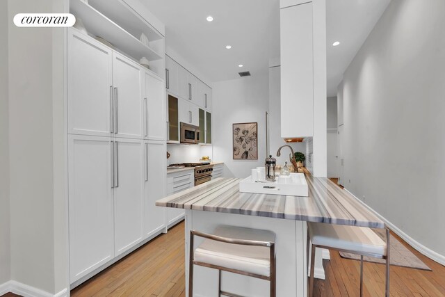 30 W 86th St Unit 2B, New York City, NY 10024 - kitchen with stainless steel appliances, a breakfast bar area, a peninsula, light wood finished floors, and white cabinetry