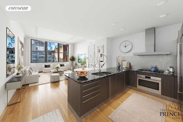 421 W 54th St Unit 4B, New York City, NY 10019 - kitchen with stainless steel oven, wall chimney range hood, a peninsula, a sink, and dark stone counters