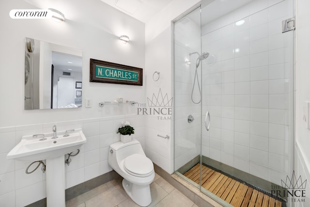 full bath with a stall shower, toilet, tile patterned flooring, and a wainscoted wall