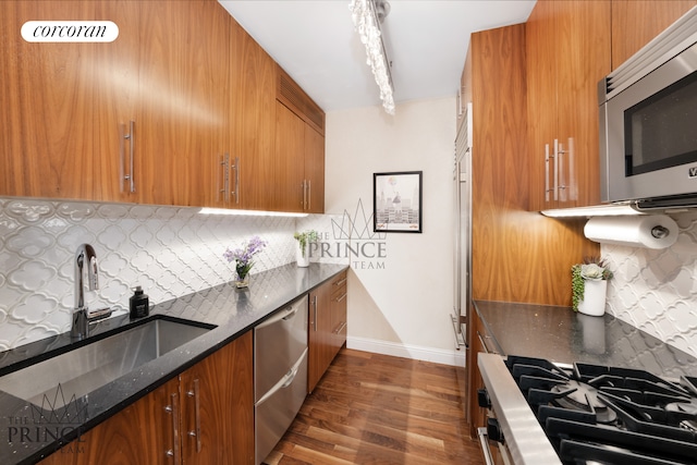 kitchen featuring dark wood-type flooring, dark stone countertops, brown cabinets, stainless steel appliances, and a sink