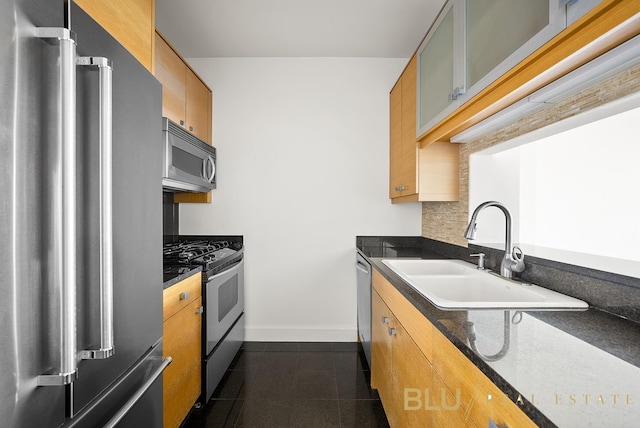 kitchen featuring baseboards, glass insert cabinets, appliances with stainless steel finishes, dark tile patterned floors, and a sink