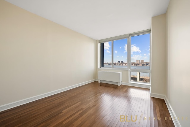 spare room featuring a view of city, dark wood finished floors, and baseboards