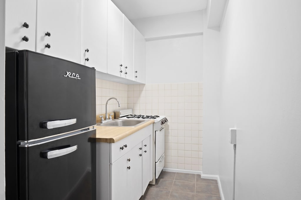 kitchen with white gas range oven, a sink, freestanding refrigerator, and white cabinets