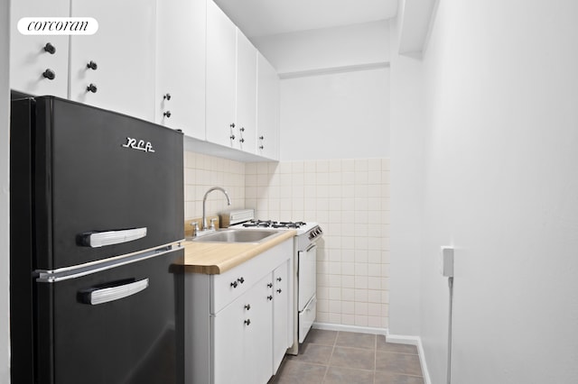 kitchen featuring light tile patterned floors, a sink, freestanding refrigerator, and white cabinetry