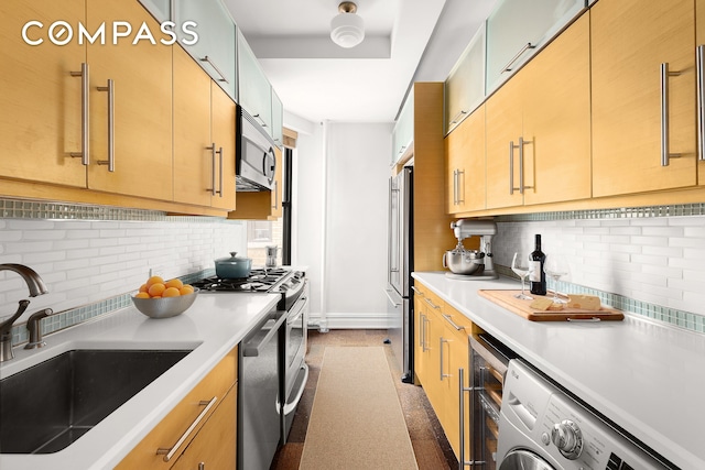 kitchen featuring washer / dryer, decorative backsplash, stainless steel appliances, light countertops, and a sink