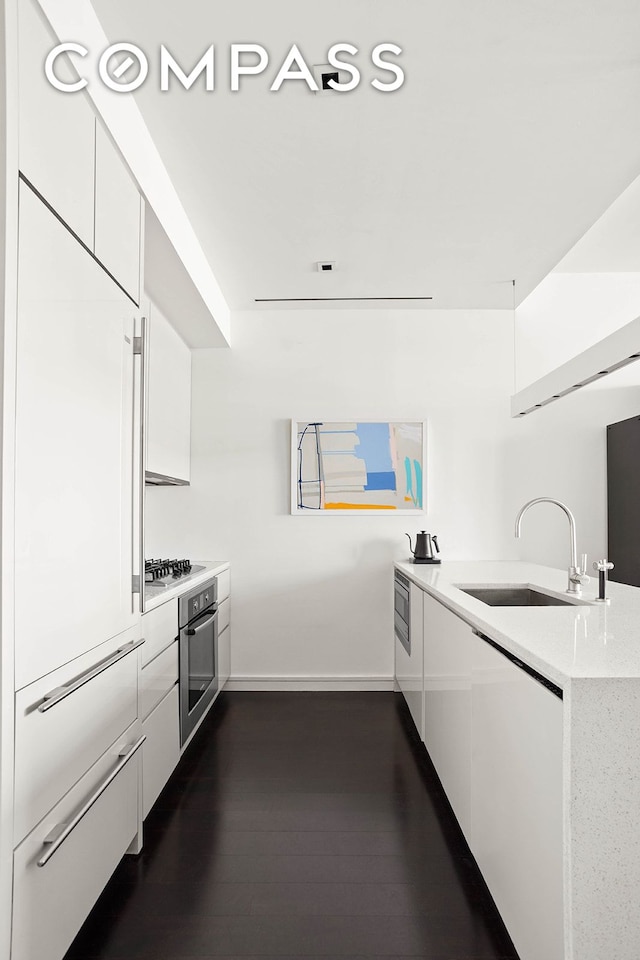 kitchen with modern cabinets, a sink, dark wood finished floors, appliances with stainless steel finishes, and white cabinets