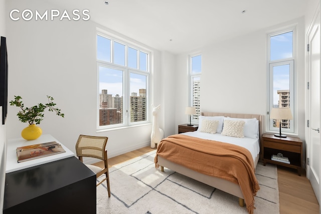 bedroom with a view of city, multiple windows, and light wood-style floors