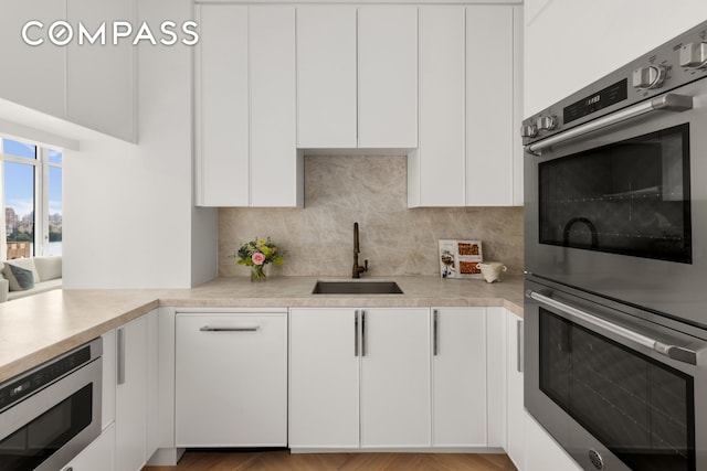 kitchen featuring backsplash, light countertops, stainless steel appliances, white cabinetry, and a sink