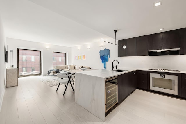 kitchen with wall oven, a sink, modern cabinets, beverage cooler, and a peninsula