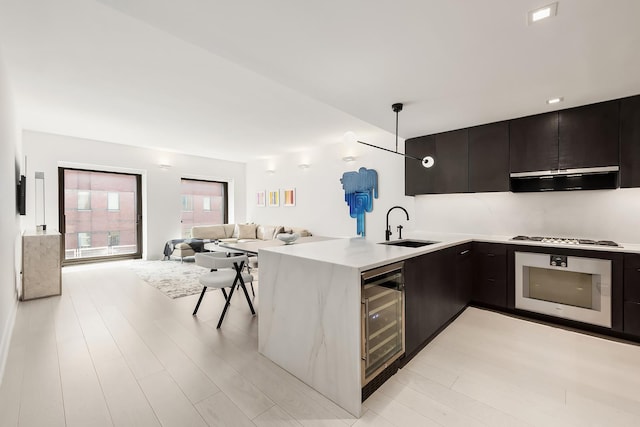 kitchen featuring modern cabinets, beverage cooler, a sink, wall oven, and a peninsula