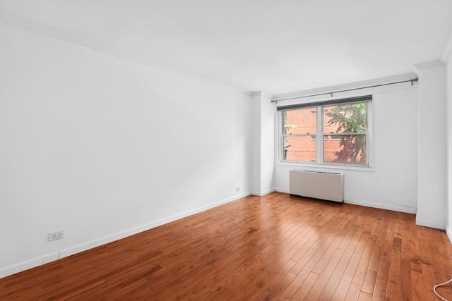 empty room featuring radiator, hardwood / wood-style flooring, baseboards, and ornamental molding