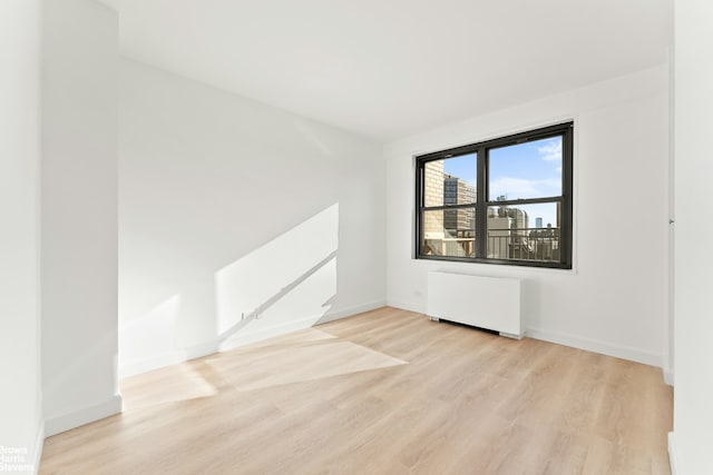 spare room featuring baseboards, wood finished floors, and radiator