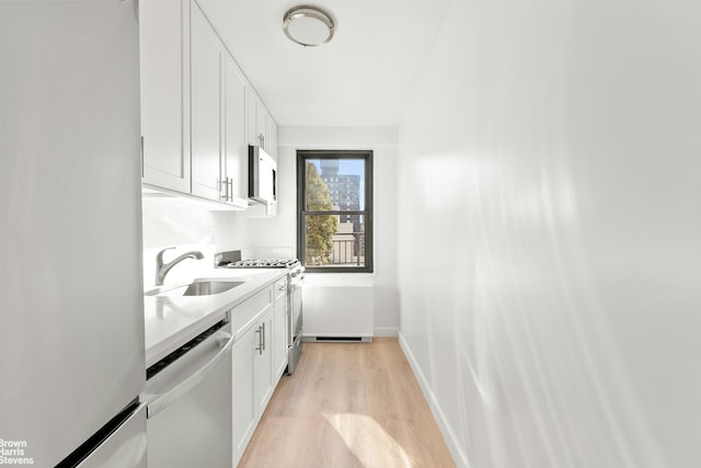 kitchen with white cabinets, appliances with stainless steel finishes, light countertops, light wood-style floors, and a sink