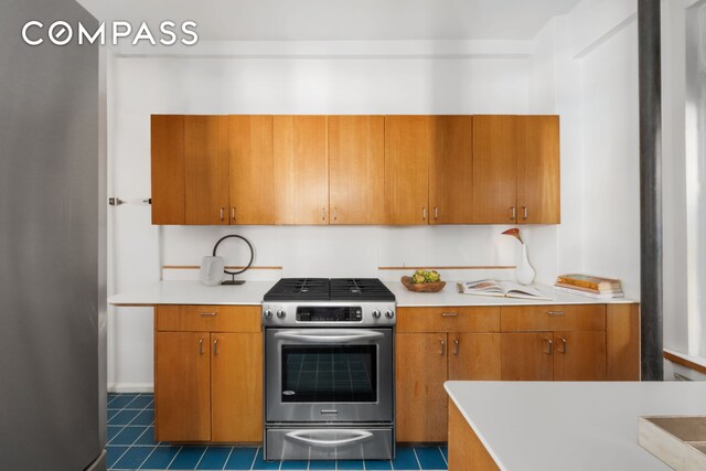 kitchen with stainless steel gas range, light countertops, brown cabinets, and dark tile patterned floors