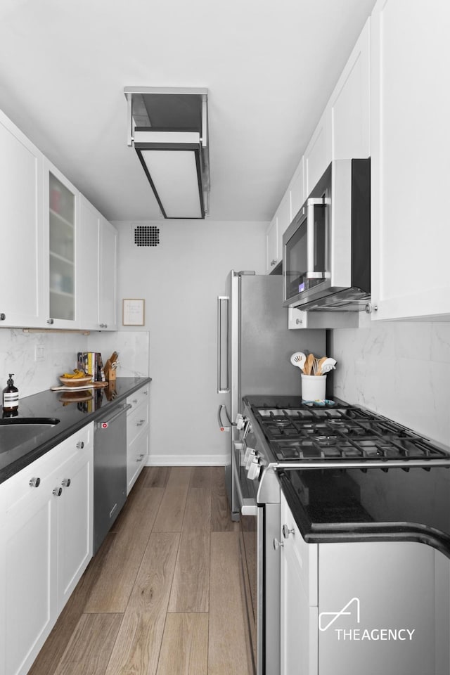 kitchen with white cabinetry, wood finished floors, stainless steel appliances, and tasteful backsplash